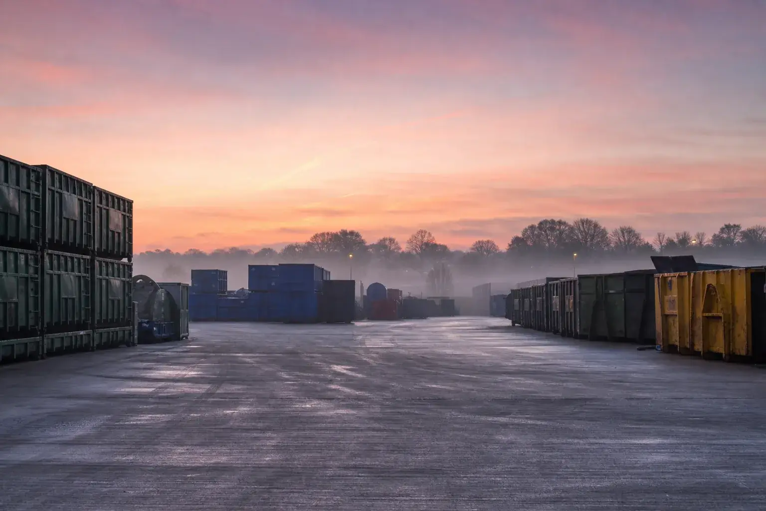 A clean waste yard at dawn with neatly stacked empty containers and swept concrete