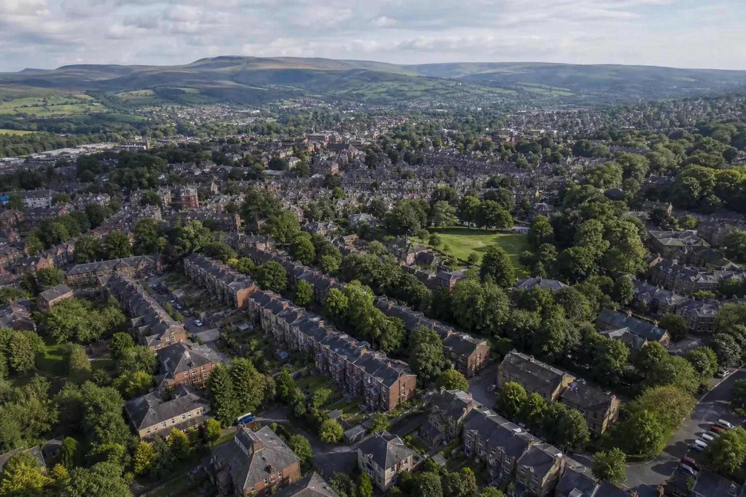 Aerial view over the rooftops and green spaces of a northern English town with the Pennine hills beyond