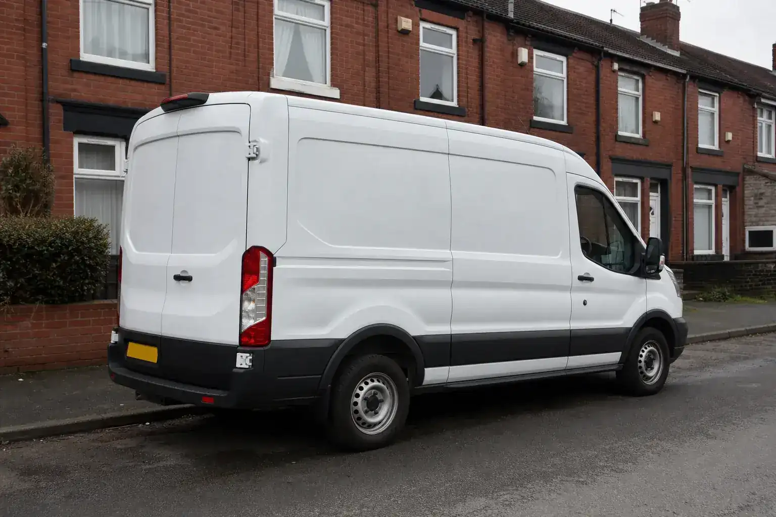 An unmarked white panel van parked on a quiet residential street of red brick terraced houses