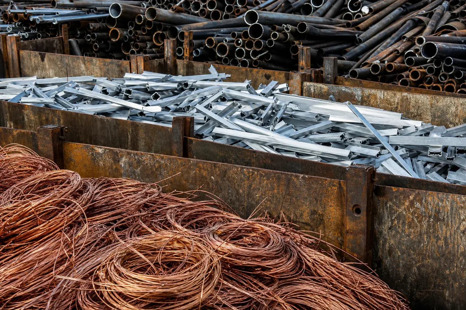 Sorted scrap metal in a recycling yard with separate bays of copper wire, aluminium and steel pipe